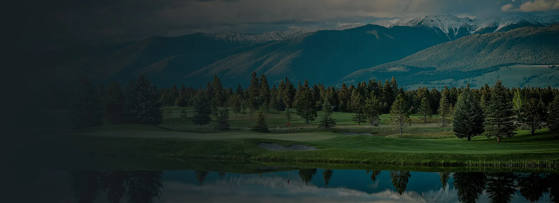 The Wilderness Club golf green reflected in water below snow-capped Montana peaks